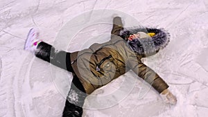 Little girl lying on the ice in skates and making a snow angel. Festive mood, Christmas, New Year, holidays, active winter sports.