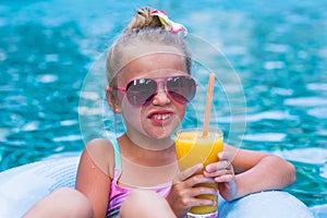 Little girl lying on inflatable ring in swimming pool. In the hands of a glass of mango juice. Holidays.