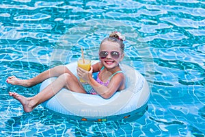Little girl lying on inflatable ring in swimming pool. In the hands of a glass of mango juice. Holidays.