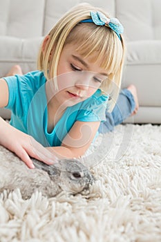 Little girl lying on rug stroking the rabbit