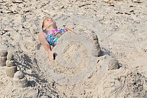 Little girl lying on the sand. Children like mummies on the beach.