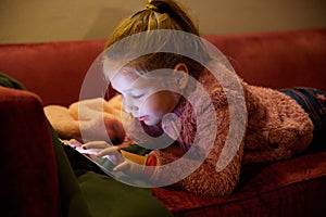 Little girl lying on sofa touching digital screen