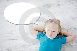 Little girl lying on white wooden floor with a speech bubble above her head