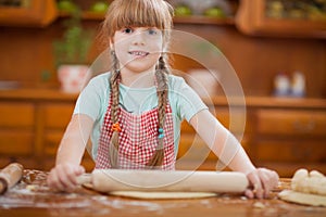 Little girl makes dough on kitchen with rolling pin