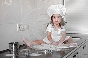 Little girl makes dough on kitchen with rolling pin