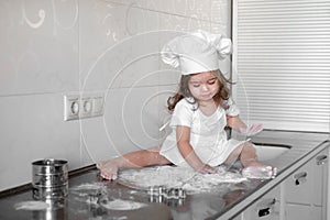 Little girl makes dough on kitchen with rolling pin