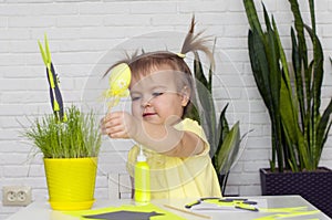 A little girl makes  Easter decorations, arranges handmade decorative elements in a pot of green grass, a Easter bunny and eggs