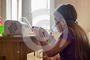 A little girl in a mask does home injections and plays a mobile game so as not to get bored.