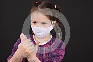 Little girl with a mask on her face washes her hands with soap