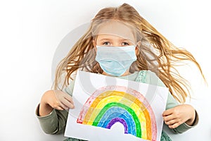 Little girl in mask holding painted rainbow during Covid-19 quarantine. Stay at home Social media campaign for coronavirus