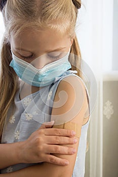 Little girl in a mask holds an arm with a plaster on the skin. Concept of vaccination