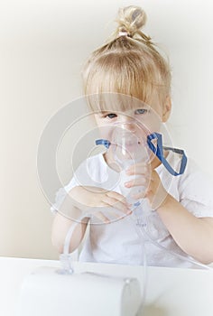 Little girl in a mask for inhalations, making inhalation with nebulizer at home inhaler on the table