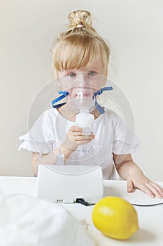 Little girl in a mask for inhalations, making inhalation with nebulizer at home inhaler on the table