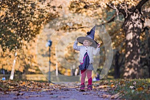 Little girl masquerade as a witch with halloween hat in sunny yellow fallen park