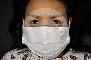 A little girl with medical mask on black background protects her from covid-19