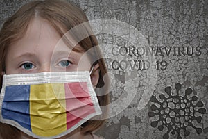 Little girl in medical mask with flag of romania stands near the old vintage wall with text coronavirus, covid, and virus picture