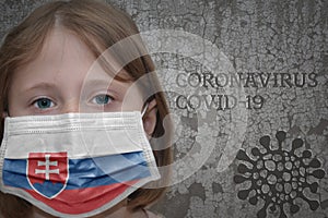 Little girl in medical mask with flag of slovakia stands near the old vintage wall with text coronavirus, covid, and virus picture