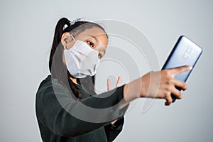 Little girl with a medical mask on his face taking a selfie with the smartphone. Concept of quarantine coronavirus infection