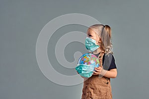 little girl in a medical mask holds a globe in her hands, wrapped in a medical mask. Little girl heals the planet