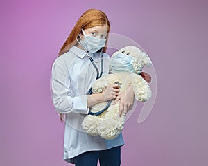 Little girl in a medical mask listens to a Teddy bear through a stethoscope. the concept of prevention covid-19