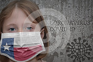 Little girl in medical mask with texas state flag stands near the old vintage wall with text coronavirus, covid, and virus picture