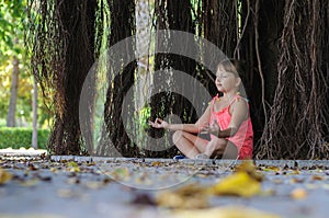 Little girl meditates under a tree