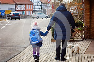 Little girl and middle aged dad on the way to elementary school. Father holding daughter, school child by hand. With