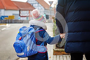 Little girl and middle aged dad on the way to elementary school. Father holding daughter, school child by hand. Happy