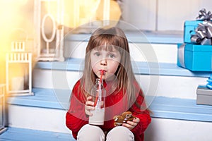 Little girl with milk and a gingerbread man sitting on porch near house. child eats cookies with milk on porch at home. Child with