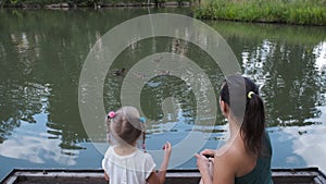 Little Girl with Mom Feeding Ducks in a City Park
