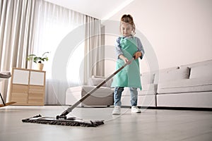 Little girl mopping floor in living room at home
