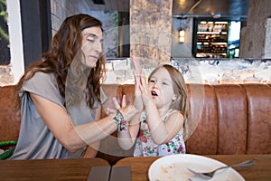 Little girl and mother in restaurant playing with hands