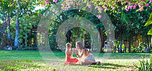 Little girl with mother sitting in the lush garden