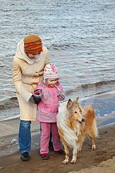 Little girl with mum and dog walk on autumn beach