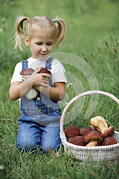 Little girl with mushrooms in hand on the green lawn