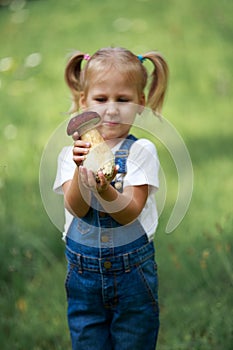 Little girl with mushrooms in hand on the green lawn