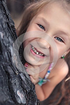 A little girl near a pine tree shows a wobbly baby tooth in her mouth