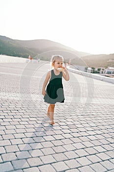 Little girl nibbles on a bun while walking barefoot on a tiled road