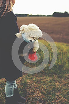 little girl observes her sorrounding wistfully with white teddy bear wearing a face mask in her arm