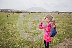 Little girl observing with binoculars nature landscape on spring day
