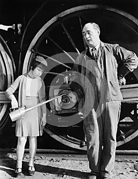 Little girl with an oil can standing next to a locomotive and the engine driver