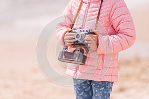 Little girl with old vintage camera making photos of sea waves and beach. Young photographer
