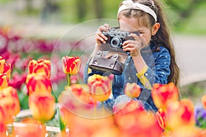 Little girl with old vintage camera making photos of tulips in flowers garden