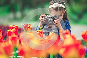 Little girl with old vintage camera making photos of tulips in flowers garden