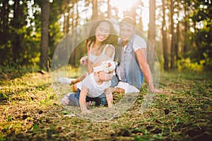 Little girl one year on the background of parents resting lying on grass learning to walk on nature in the park. The first steps