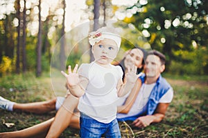 Little girl one year on the background of parents resting lying on grass learning to walk on nature in the park. The first steps