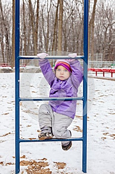 Little girl one year old climbing the ladder outside in winter park playground.