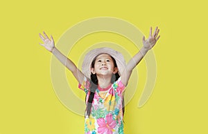 Little girl open arms wide with looking up isolated on yellow background. Kid in floral pattern summer dress and hat. Holiday and