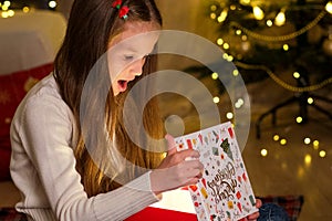 Little girl opening Christmas gift on background of Christmas Tree at home