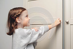 Little girl opens the cupboard. Cute baby girl playing with a wooden cupboard. A small child opens a shelf drawer